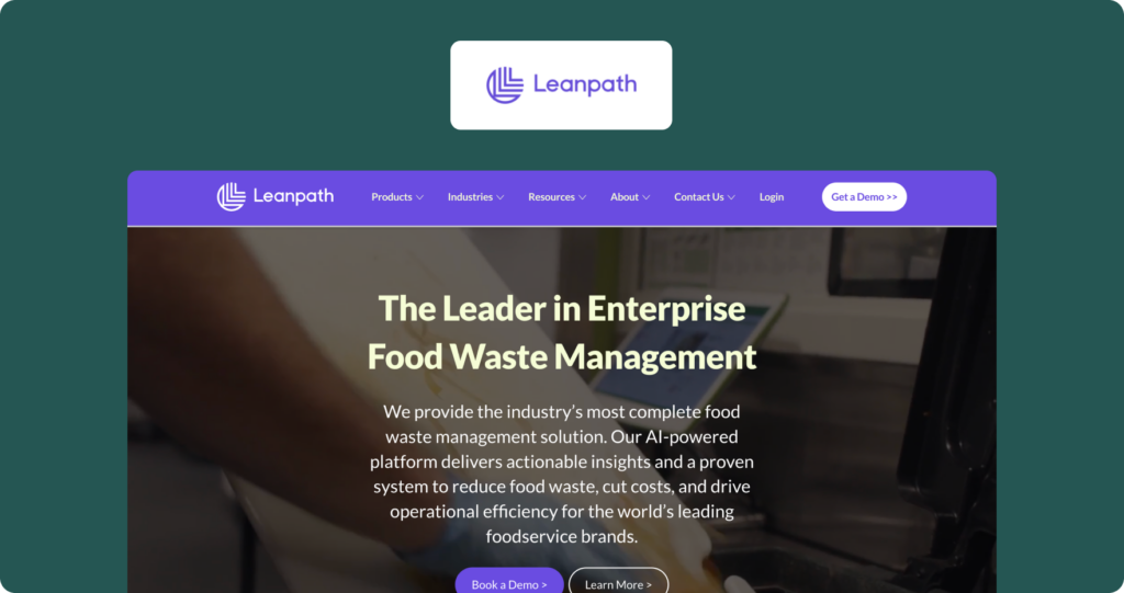 A screenshot of the Leanpath website homepage, showing the Leanpath logo in a white card above a hero section with a dark kitchen background. The hero headline reads "The Leader in Enterprise Food Waste Management," with supporting copy describing an AI-powered platform that delivers actionable insights to reduce food waste, cut costs, and drive operational efficiency for foodservice brands. Purple "Book a Demo" and dark "Learn More" CTA buttons appear at the bottom, set against a teal-green page background.