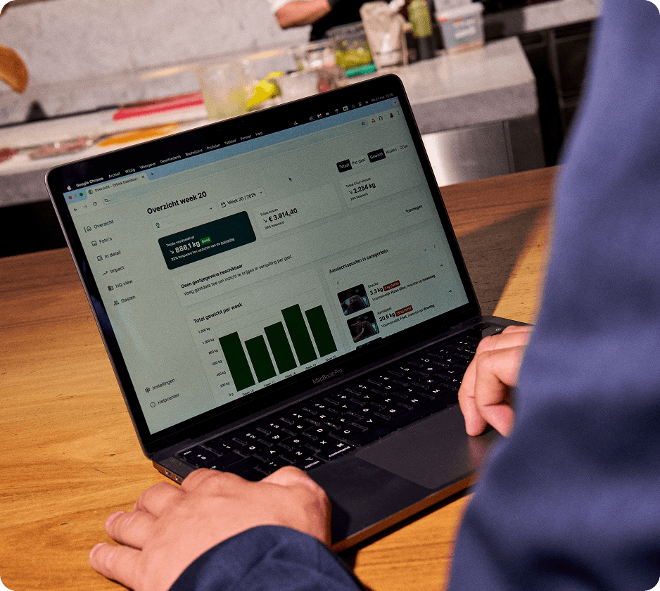 orbisk-dashboard-laptop Laptop met het Orbisk-dashboard voor voedselverspilling, met wekelijkse verspillingstotalen en een kostenoverzicht, in een café